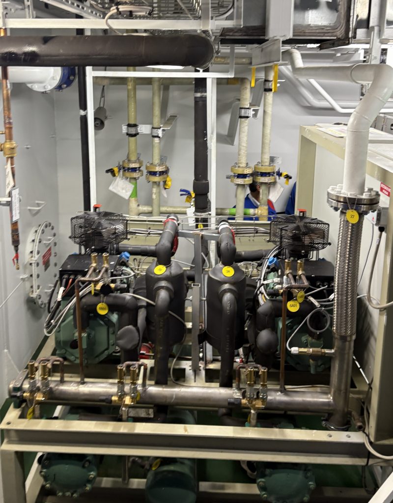 A close-up view of a mechanical room featuring multiple pumps, pipes, and cooling fans, arranged on a metal frame with identifying labels.